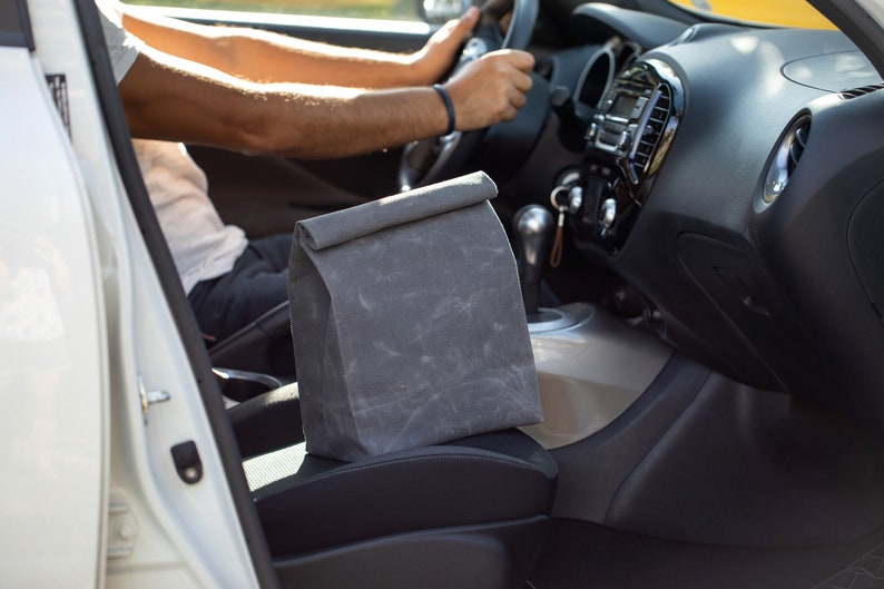 May include: A gray fabric lunch bag sits on the passenger seat of a white car.