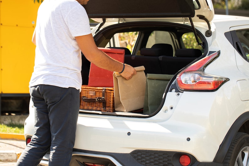 May include: A person loading a white car with a wicker basket, a red canvas bag, a brown canvas bag, and a green canvas bag.