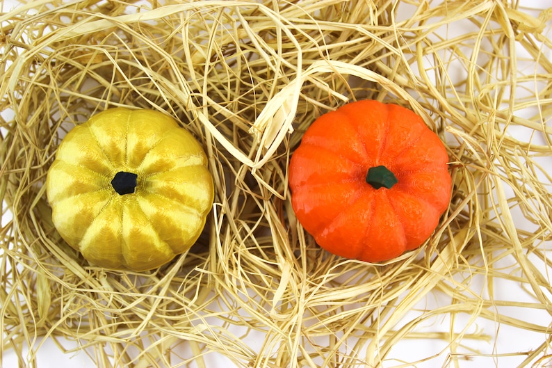 May include: Two decorative pumpkins, one yellow and one orange, are nestled in a bed of straw.