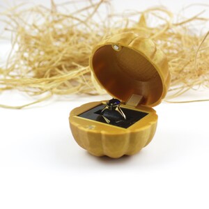 May include: A gold ring box shaped like a pumpkin with a blue gemstone ring inside.