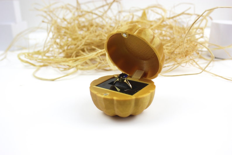 May include: A gold ring box shaped like a pumpkin with a blue gemstone ring inside.
