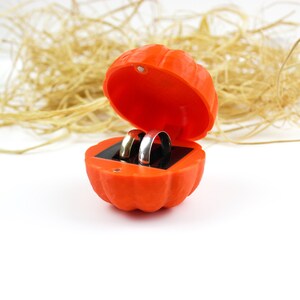 May include: Two gold wedding bands inside an orange pumpkin-shaped ring box.
