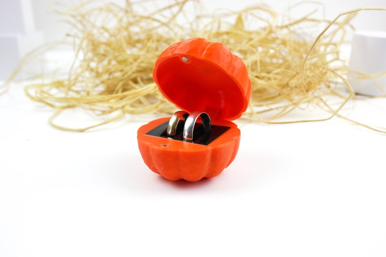 May include: Two gold wedding bands inside an orange pumpkin-shaped ring box.