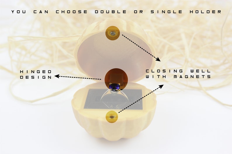 May include: A wooden ring box with a hinged design. The box is shaped like a seashell and has a velvet interior. The box closes with magnets. "You can choose double or single holder" is written on the top of the box.
