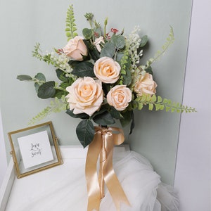 May include: A bridal bouquet with peach roses and greenery, tied with a gold satin ribbon.