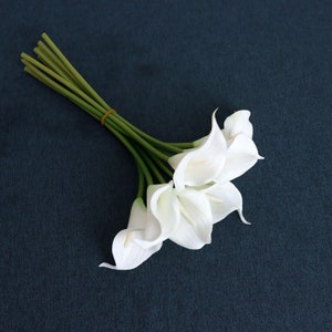 May include: A bouquet of white artificial calla lilies with green stems tied together with a rubber band.