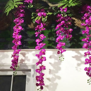 May include: A string of artificial purple orchid flowers hanging from a branch. The flowers are in bloom and have a realistic appearance.