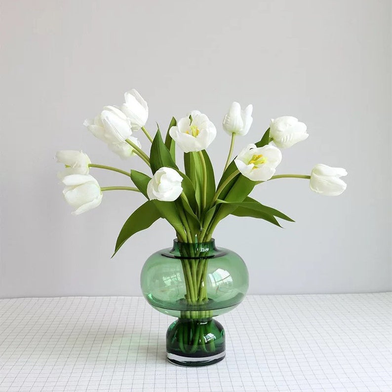 May include: A bouquet of white tulips arranged in a green glass vase with a round body and a flared base.