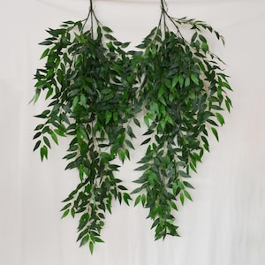 May include: Two hanging artificial willow branches featuring long, slender stems covered in numerous pointed, vibrant green leaves. The foliage is arranged in a cascading, downward-flowing pattern, creating a dense and lush appearance for decor.