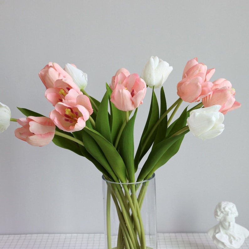 May include: A bouquet of pink and white artificial tulips in a clear glass vase. The tulips are arranged in a vase with green stems.
