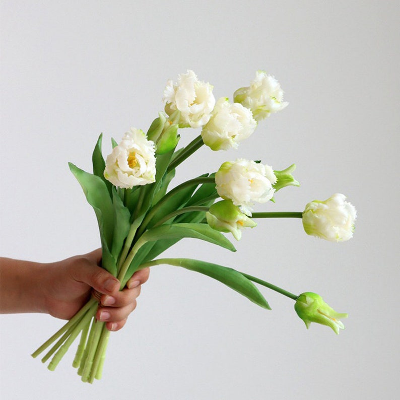 Op de afbeelding: Een boeket witte kunsttulpen met groene stelen. De tulpen hebben gekrulde bloemblaadjes en zijn gerangschikt in een handboeket.