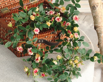 Puede incluir: Una larga guirnalda de rosas artificiales de color rosa y blanco con hojas verdes. La guirnalda está drapeada sobre una cesta de mimbre.
