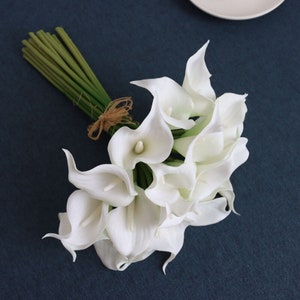 May include: A bouquet of white calla lilies with green stems tied together with twine.