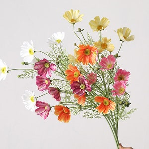 Könnte beinhalten: Ein Strauß künstlicher Blumen mit weißen, gelben, orangefarbenen und rosa Blütenblättern. Die Blumen sind zu einem Strauß gebunden und haben grüne Stiele.