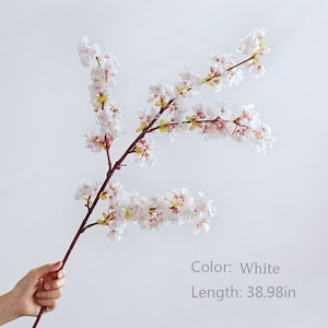 May include: A single white artificial cherry blossom branch with pink accents. The branch is 38.98 inches long.