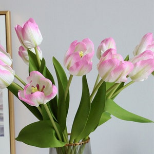 May include: A bouquet of pink and white artificial tulips with green stems in a clear glass vase with a gold rim.