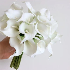 May include: A bouquet of white calla lilies with green stems. The flowers are arranged in a cluster and are ready to be used for a wedding or other special occasion.