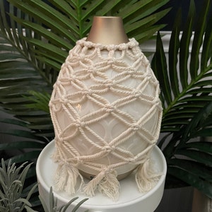 Op de afbeelding: Witte keramische etherische olieverdamper met een crèmekleurige gehaakte hoes en een gouden bovenkant. De diffuser staat op een witte tafel.