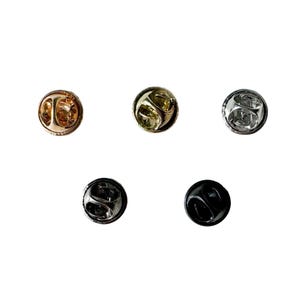 May include: Five pin back closures in different finishes: gold, silver, black, and two shades of bronze.