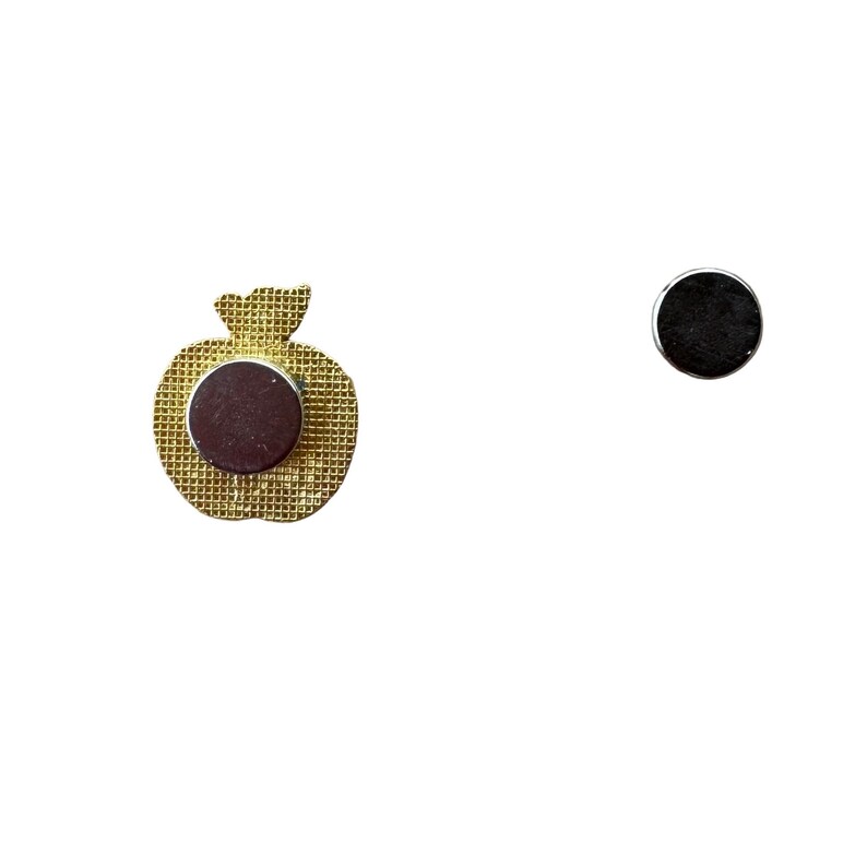 May include: A gold-coloured apple-shaped magnet with a dark brown magnetic backing. A separate, round, black magnet is also visible. The apple magnet has a textured surface and a small stem.