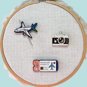Airplane, ticket and camera magnetic needle minders – travel themed enamel accessory for cross stitch, embroidery, and needlepoint – fun stitching gift for travelers and adventure lovers.