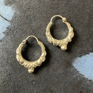 Pode incluir: Um par de brincos de argola de prata com um design intrincado e texturizado. Os brincos têm uma pequena pérola redonda na parte inferior.