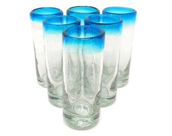 May include: Set of six clear glass shot glasses with a blue rim. The glasses are arranged in a semi-circle.