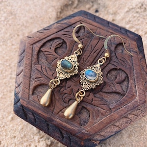May include: A pair of gold dangle earrings with a teardrop-shaped pendant and a round, iridescent gemstone set in a filigree design.