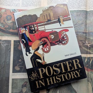 May include: A book titled "The Poster in History" by Max Gallo. The cover features a vintage red car with passengers, and figures in period clothing. The background includes a building and a landscape. The book is on a newspaper background.