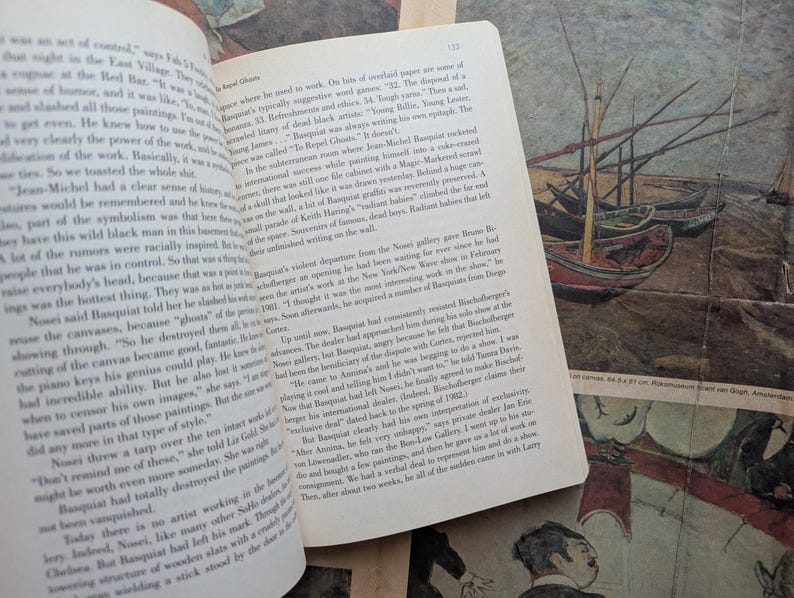 Puede incluir: Un libro abierto con texto en la p&aacute;gina izquierda y una pintura de barcos en la derecha. La pintura tiene una est&eacute;tica vintage, con un aspecto descolorido. El libro est&aacute; sobre una superficie estampada.