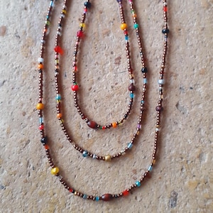 May include: Three layered beaded necklaces with copper-colored chains. The necklaces feature a variety of colorful beads, including red, yellow, blue, and white. The beads are small and round, creating a delicate and intricate design.