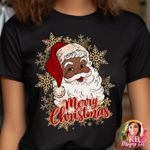 May include: Black t-shirt featuring a graphic of Santa Claus with a red hat and the words "Merry Christmas" in red script. Gold snowflakes surround Santa's face, creating a festive holiday design.
