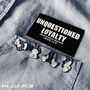May include: Four black and white enamel pins with a Star Wars theme. The pins depict the hand gestures of the Imperial Stormtroopers. The pins are displayed on a blue denim shirt with a black card that reads "Unquestioned Loyalty" in white text.