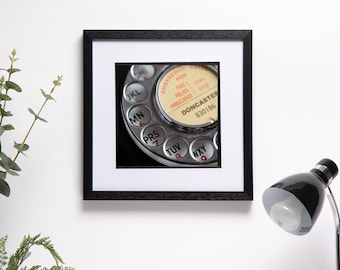 May include: A close-up of a vintage rotary dial telephone with a silver face and black background. The dial has the letters JKL, MN, PRS, TUV, and WXY printed on it. The dial also has a yellow sticker with the text "EMERGENCY FOR FIRE POLICE AMBULANCE DIAL 999 DONCASTER 830186".