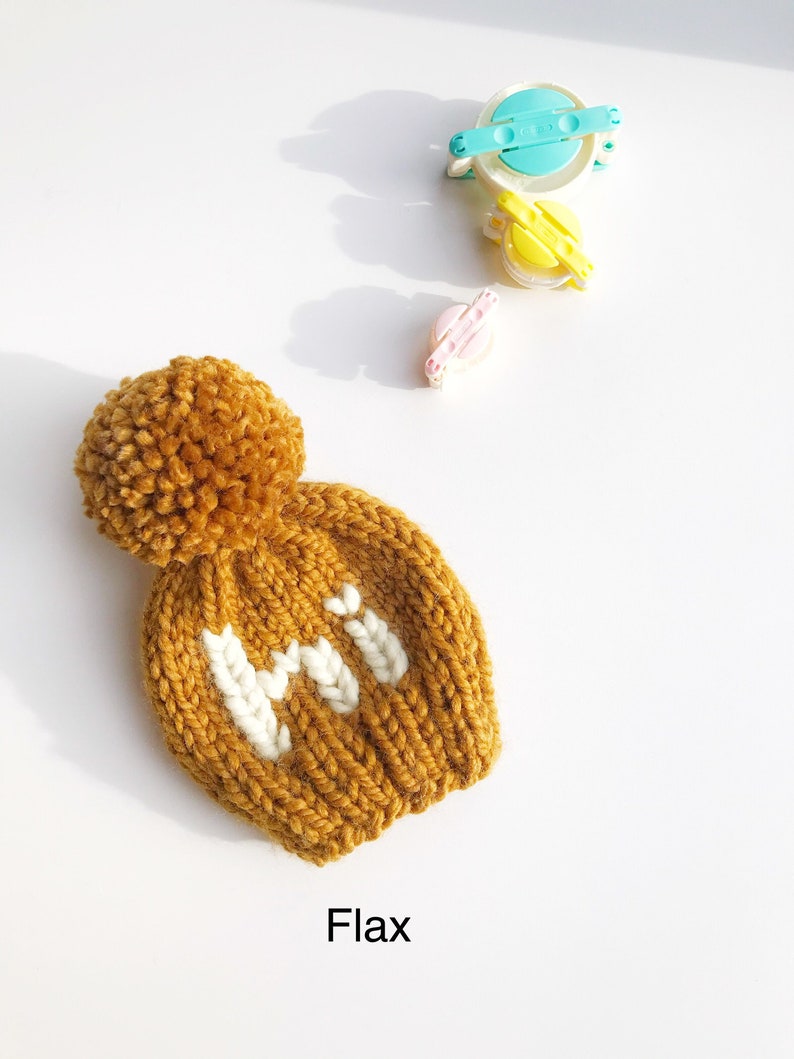 May include: A knitted hat with a pom pom on top. The hat is mustard yellow with white knit letters that spell "HI".