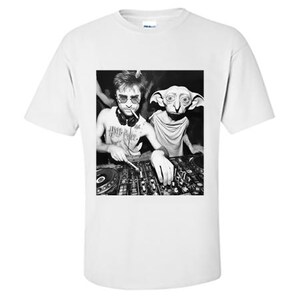 May include: White t-shirt featuring a black and white image of two figures at a DJ setup. One figure wears sunglasses and has a tattoo that says "Harry Potter". The other figure is a house elf. The shirt is a Gildan brand.