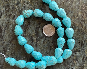 May include: A strand of turquoise blue gemstone beads, each bead is faceted and shaped like a teardrop. The beads are strung on a white cord and are arranged in a double row.