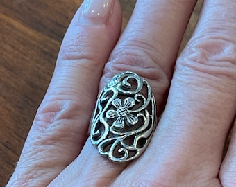 May include: A silver ring with a floral design. The ring is oval shaped and has a delicate, intricate design.