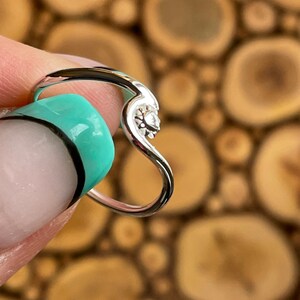 Könnte beinhalten: Ein silberner Ring in Herzform mit einem kleinen, klaren Stein in der Mitte.