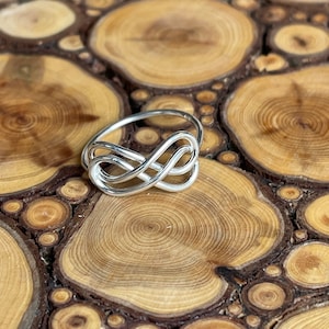 May include: A silver infinity knot ring on a wooden background.