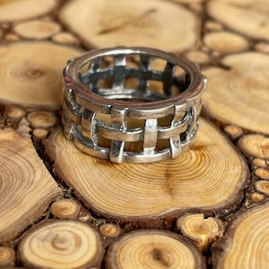 May include: A silver ring with a woven design. The ring is sitting on a wooden surface.