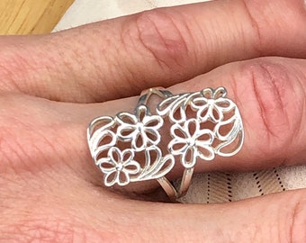 May include: A silver ring with a delicate floral design. The ring features a cluster of stylized flowers with openwork details.