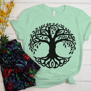 May include: A light green t-shirt with a black tree of life design. The tree has a thick trunk and many branches with leaves. The roots of the tree are intertwined and form a circle around the trunk.
