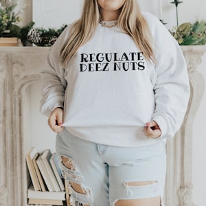 May include: A white sweatshirt with the text "REGULATE DEEZ NUTS" printed in black.