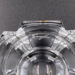May include: Close-up of the bottom of a clear glass bowl with a cut-glass design. The bowl has a signature that reads "Baccarat" on the bottom.