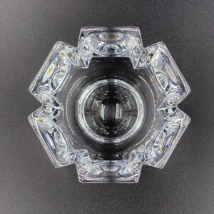 May include: A clear glass ashtray with a geometric design. The ashtray has a hexagonal shape with eight sides and a deep bowl.