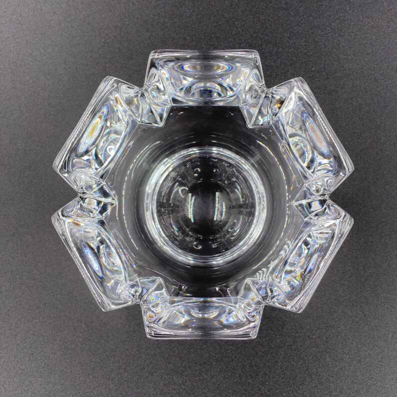 May include: A clear glass ashtray with a geometric design. The ashtray has a hexagonal shape with eight sides and a deep bowl.