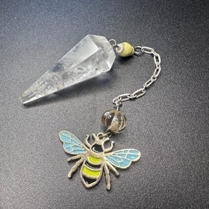 Può includere: Un pendolo di cristallo di quarzo trasparente con una catena d'argento e un ciondolo decorativo a forma di ape. Il ciondolo a forma di ape presenta dettagli in smalto blu, giallo e nero. Il pendolo è progettato per la divinazione.