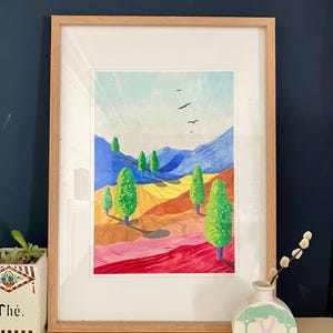 Puede incluir: Un cuadro de paisaje enmarcado que presenta colinas onduladas y estilizadas en tonos rojos, naranjas y amarillos, salpicadas de cipreses de color verde brillante. El fondo muestra montañas azules bajo un cielo pálido con tres aves negras.