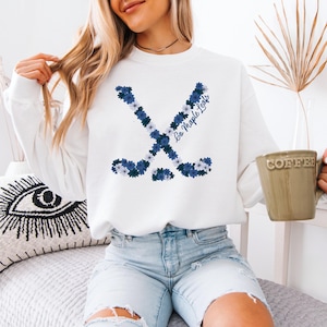 May include: White sweatshirt with a floral hockey stick design in blue and white. The words "Go Maple Leafs" are written in script. The sweatshirt has a crew neck and is a casual style.